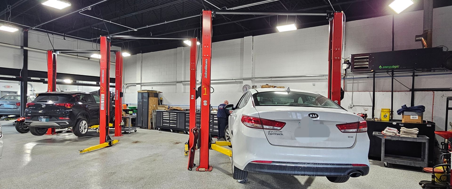 Cars on lifts in a mechanics shop, red lift posts, one worker, tools, and lights.