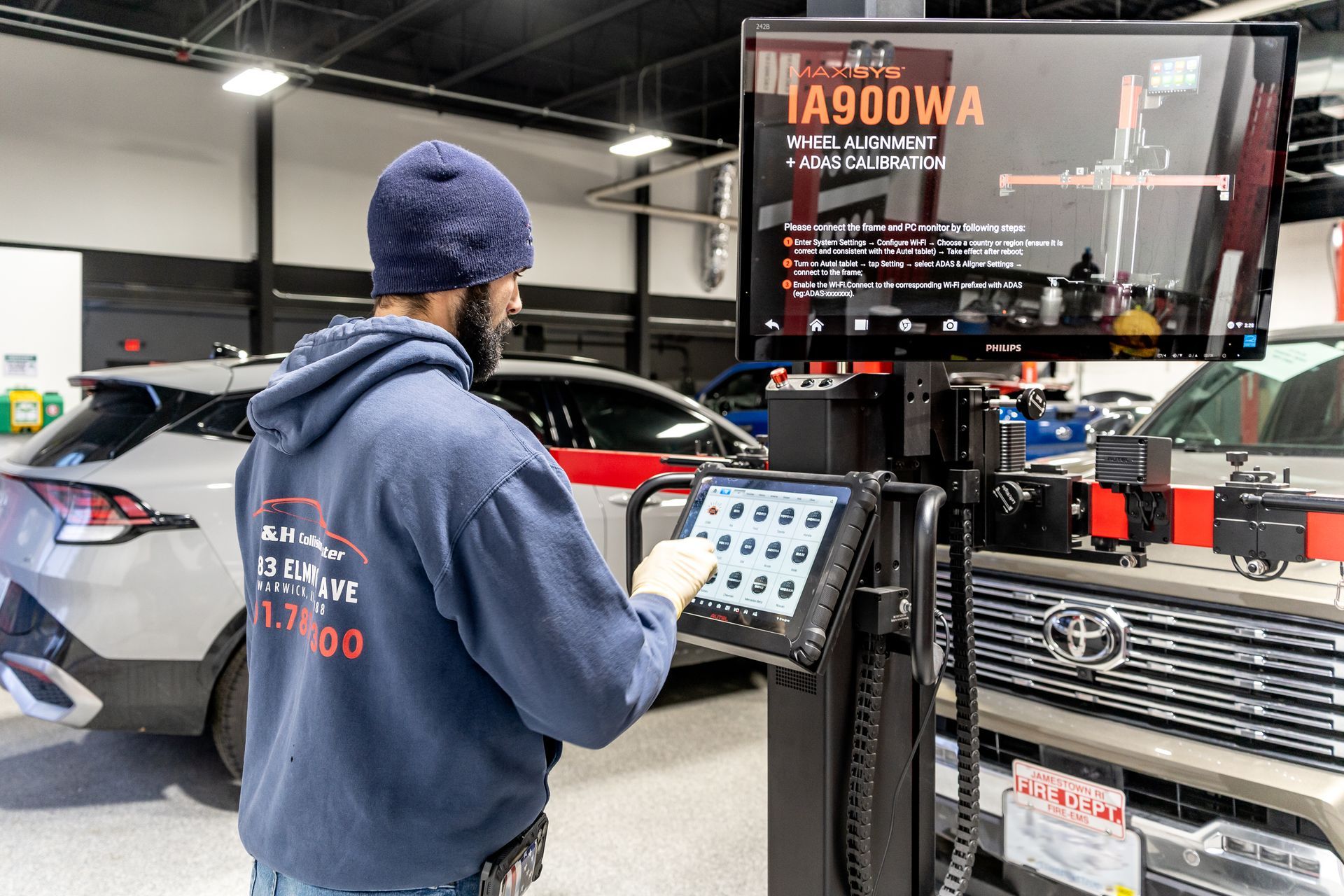 Mechanic using a tablet to analyze a car's alignment, with a large screen displaying data.