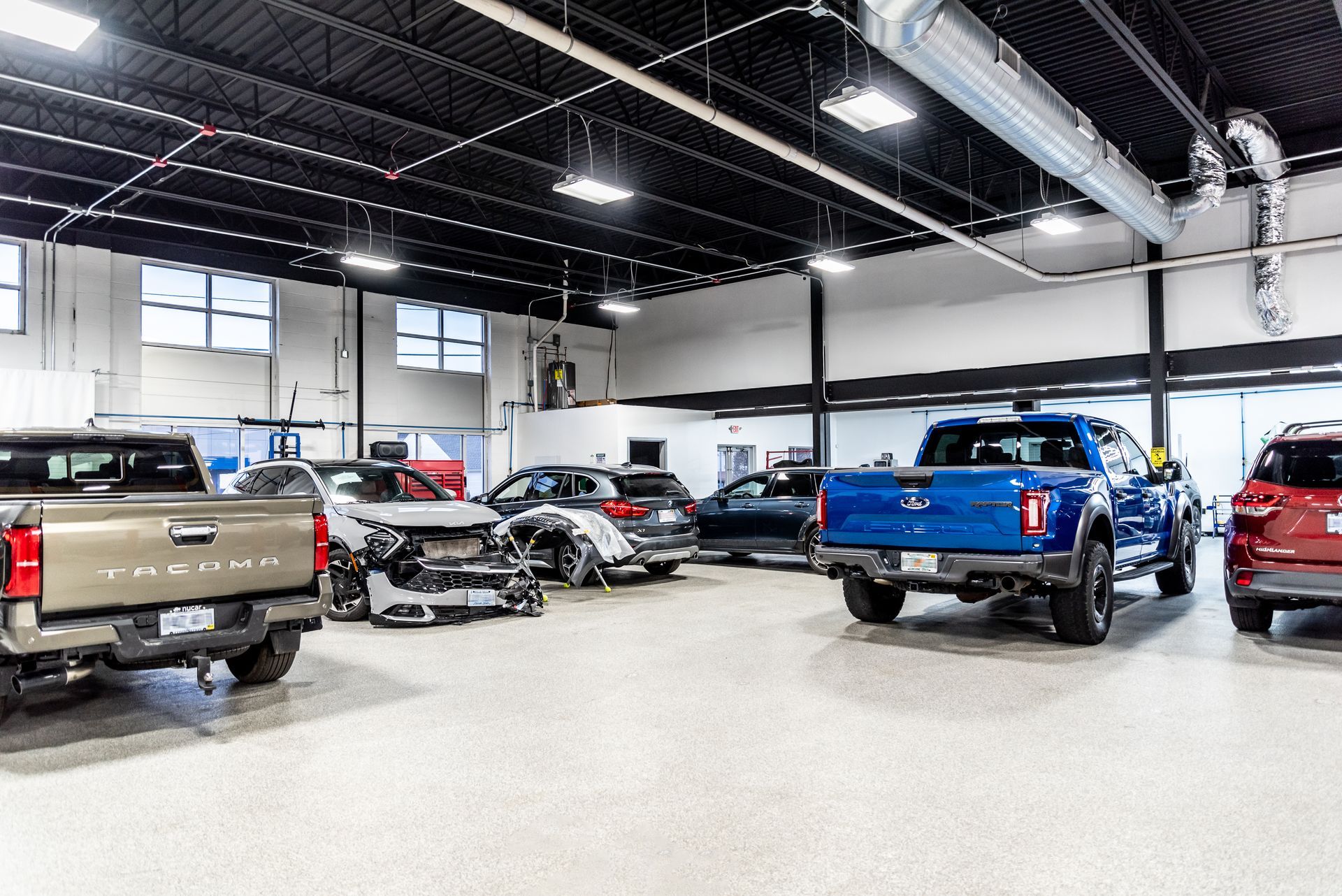 Cars inside a large auto repair shop. Includes trucks and other vehicles. Overhead lighting is present.