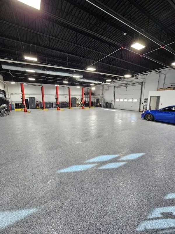 A large, bright auto repair shop interior with several car lifts and a blue car parked inside.