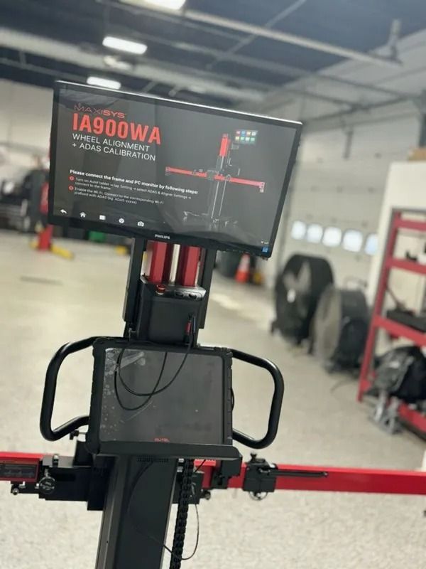 Alignment machine, red and black, in a garage. Large screen displays calibration instructions.