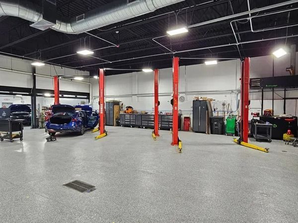 Inside a garage with red car lifts, a blue car being worked on. Other tools and cabinets visible.