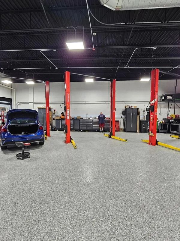 Interior of an auto repair shop with four red lifts, a blue car, and a person working at a bench.