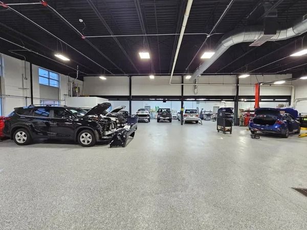 Cars in a car repair shop with open hoods and visible damage. The setting is indoors, with a grey floor.