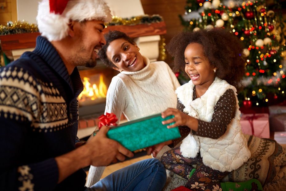 Family exchanging Christmas gifts near a decorated tree and fireplace.
