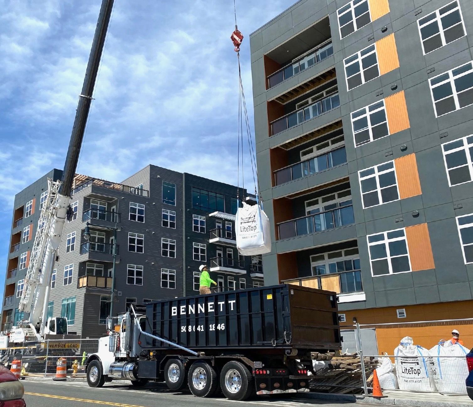 Construction trucks outside gray apartment buildings on a city street under a cloudy sky