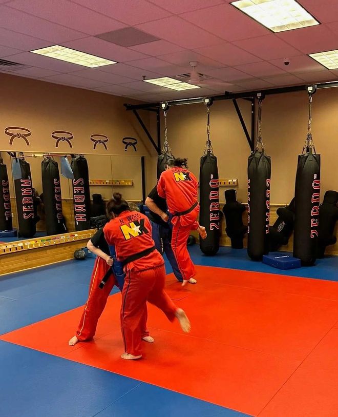 People in red uniforms practicing martial arts on a red mat in a dojo.