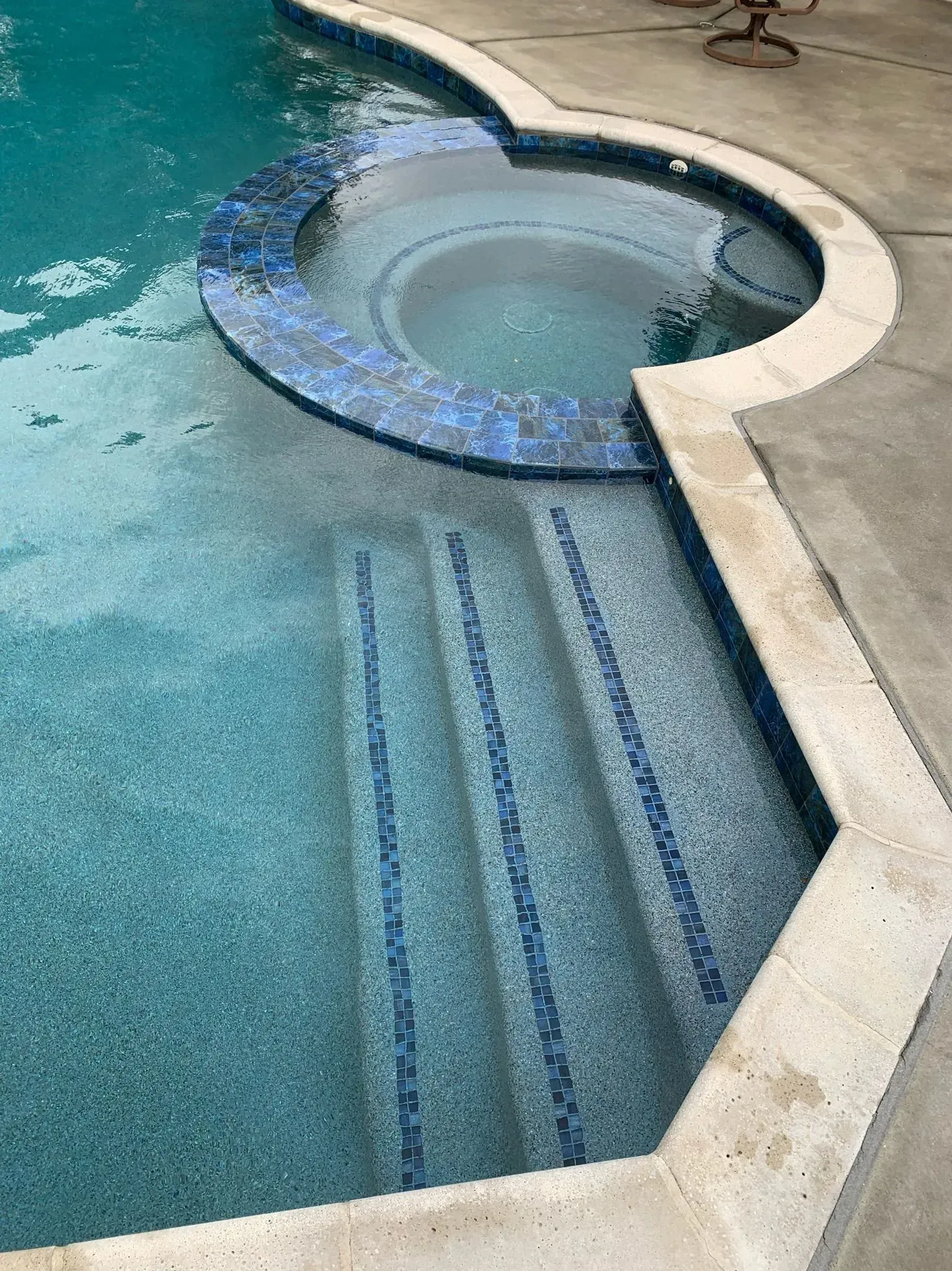 Pool with steps, a spa with blue mosaic tile, and a concrete deck.