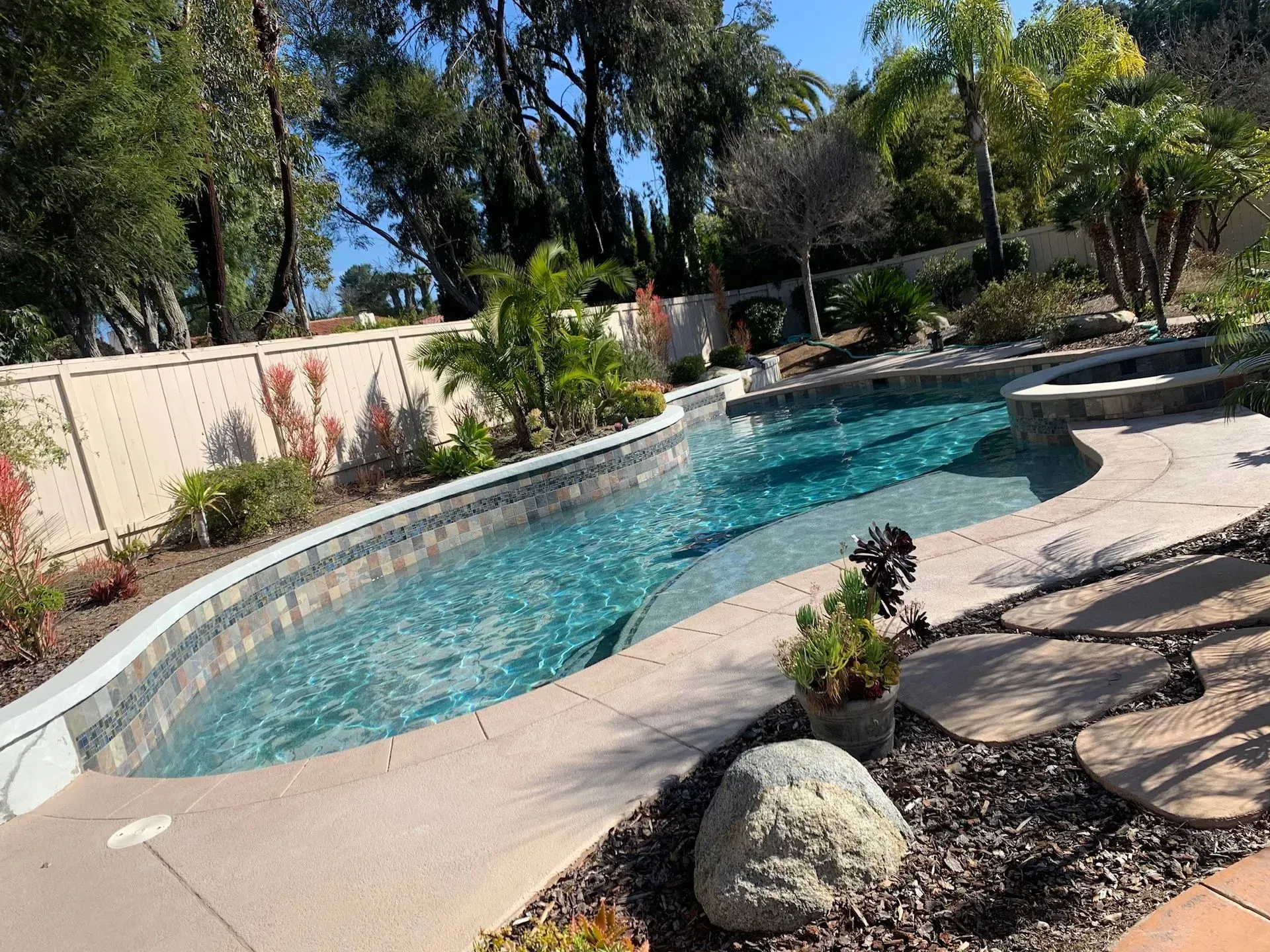 Swimming pool in a backyard with landscaping, trees, and a spa.
