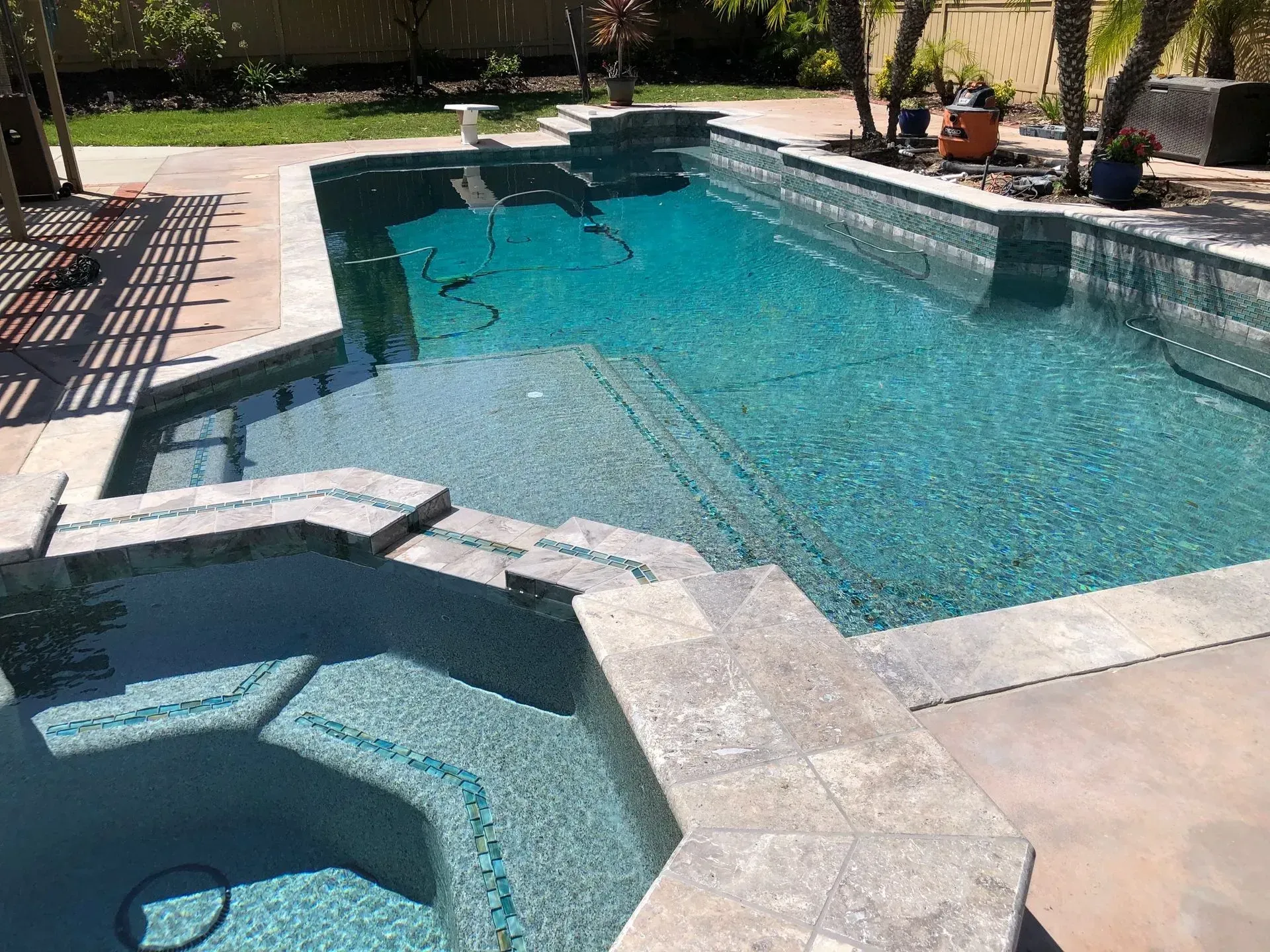 Swimming pool with turquoise water, built-in spa, and stone steps and border, outdoors.