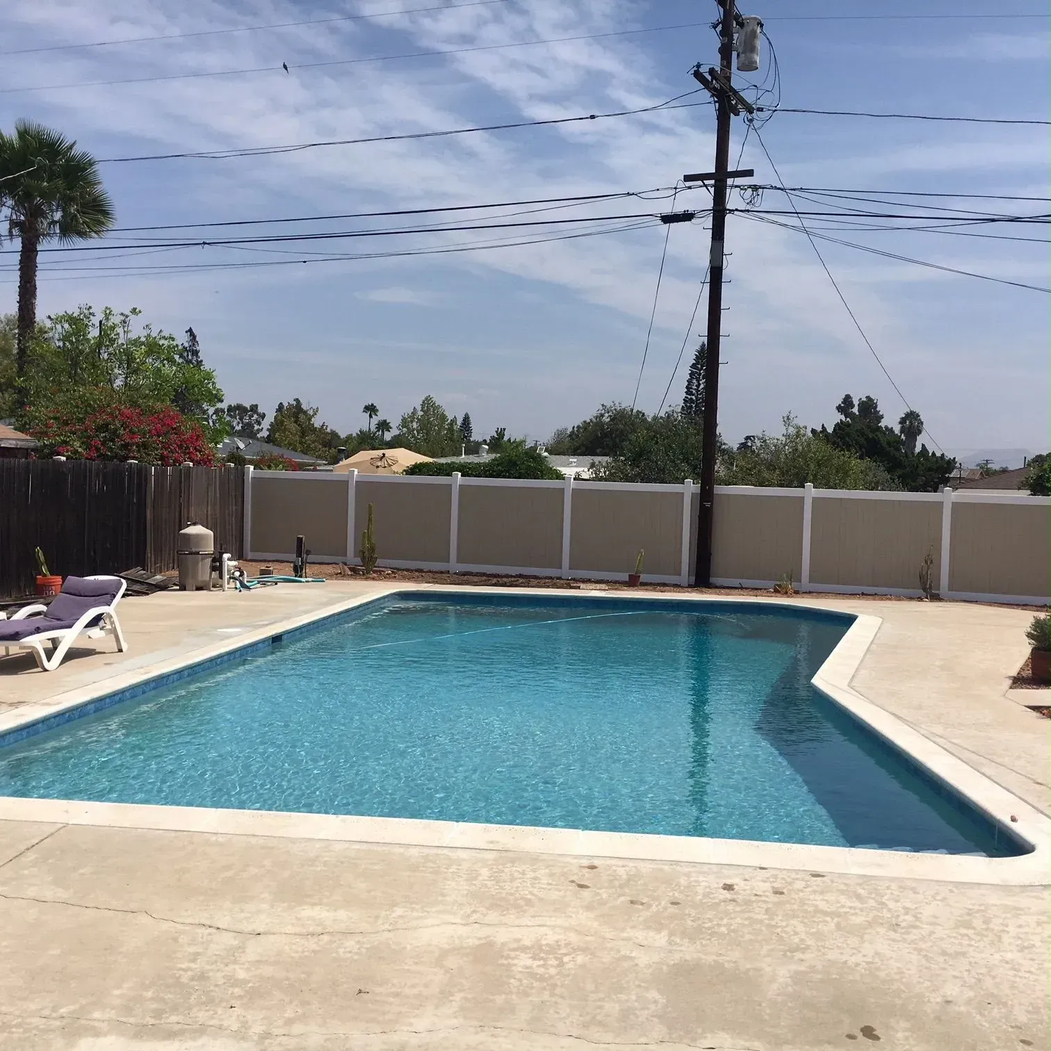 Swimming pool surrounded by concrete, fence, and a clear, sunny sky.