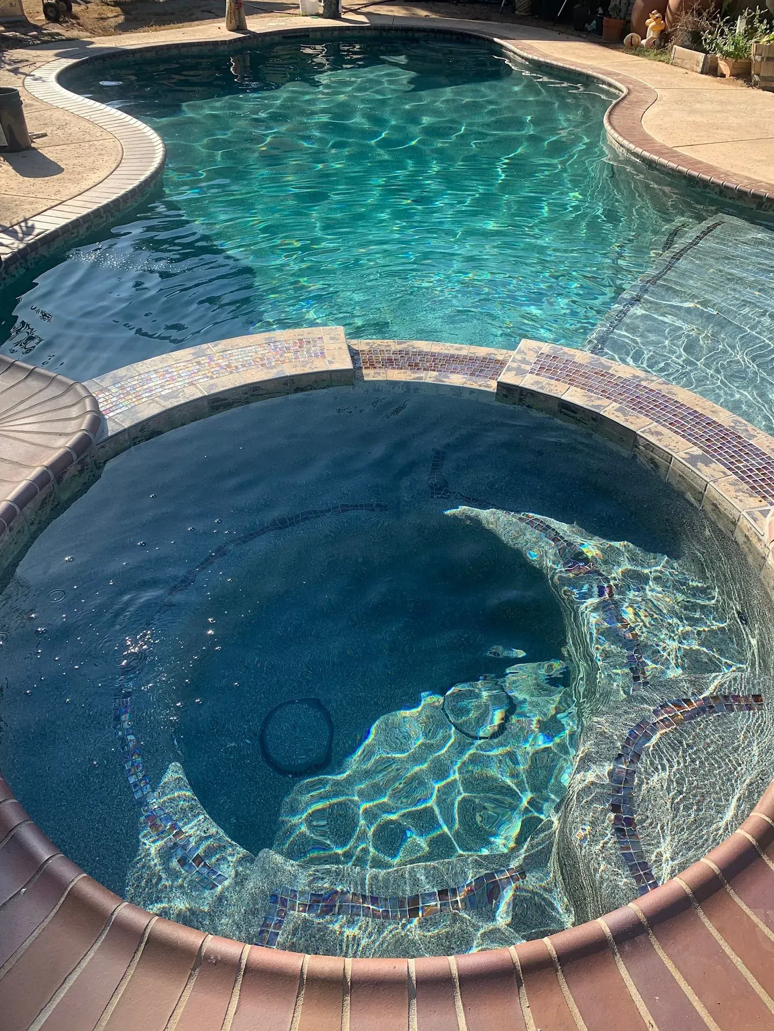 Swimming pool and connected hot tub; turquoise water, stone coping, sunny outdoor setting.