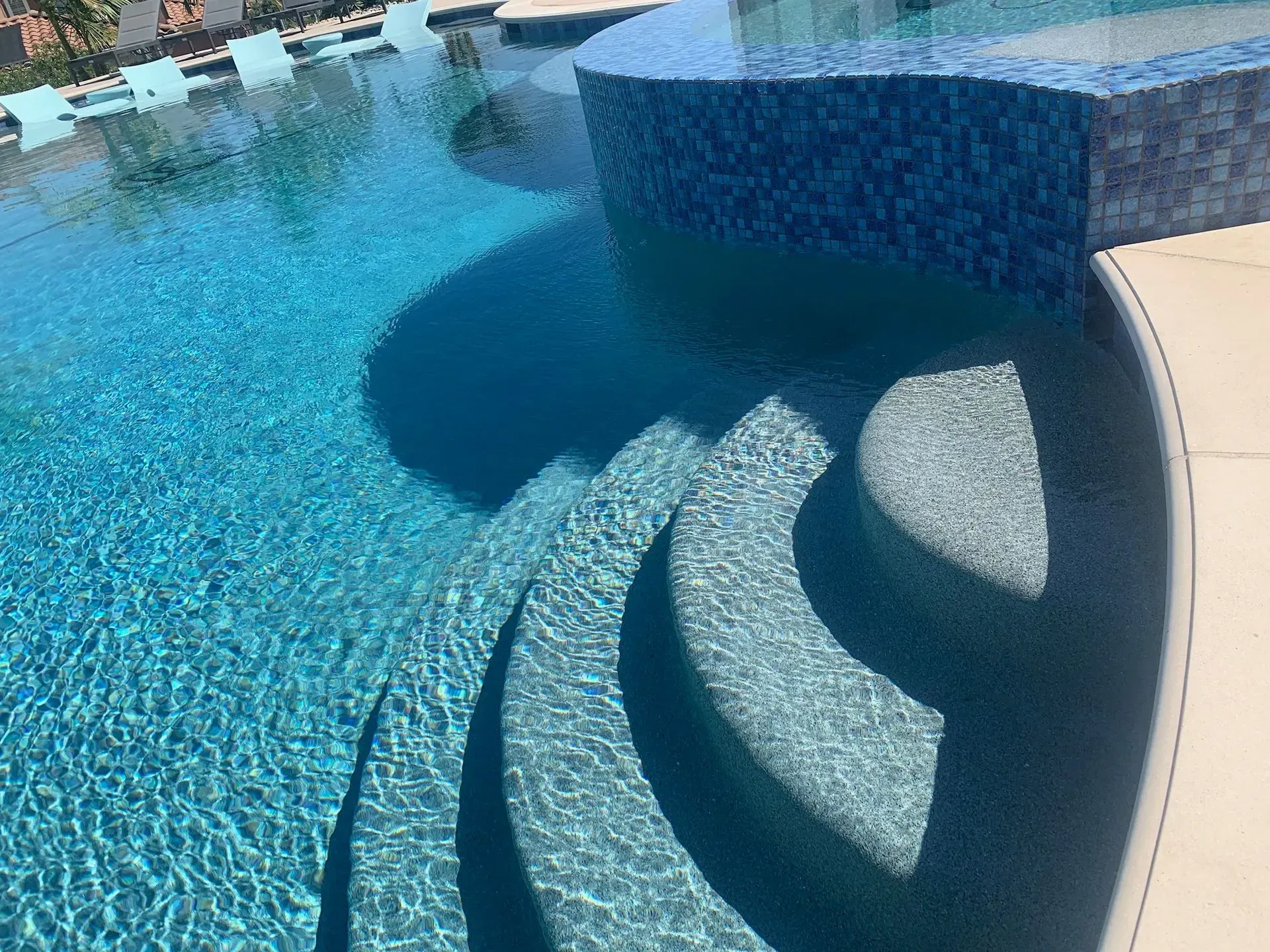 Swimming pool with built-in steps and a raised, tiled spa section; blue water, sunny day.