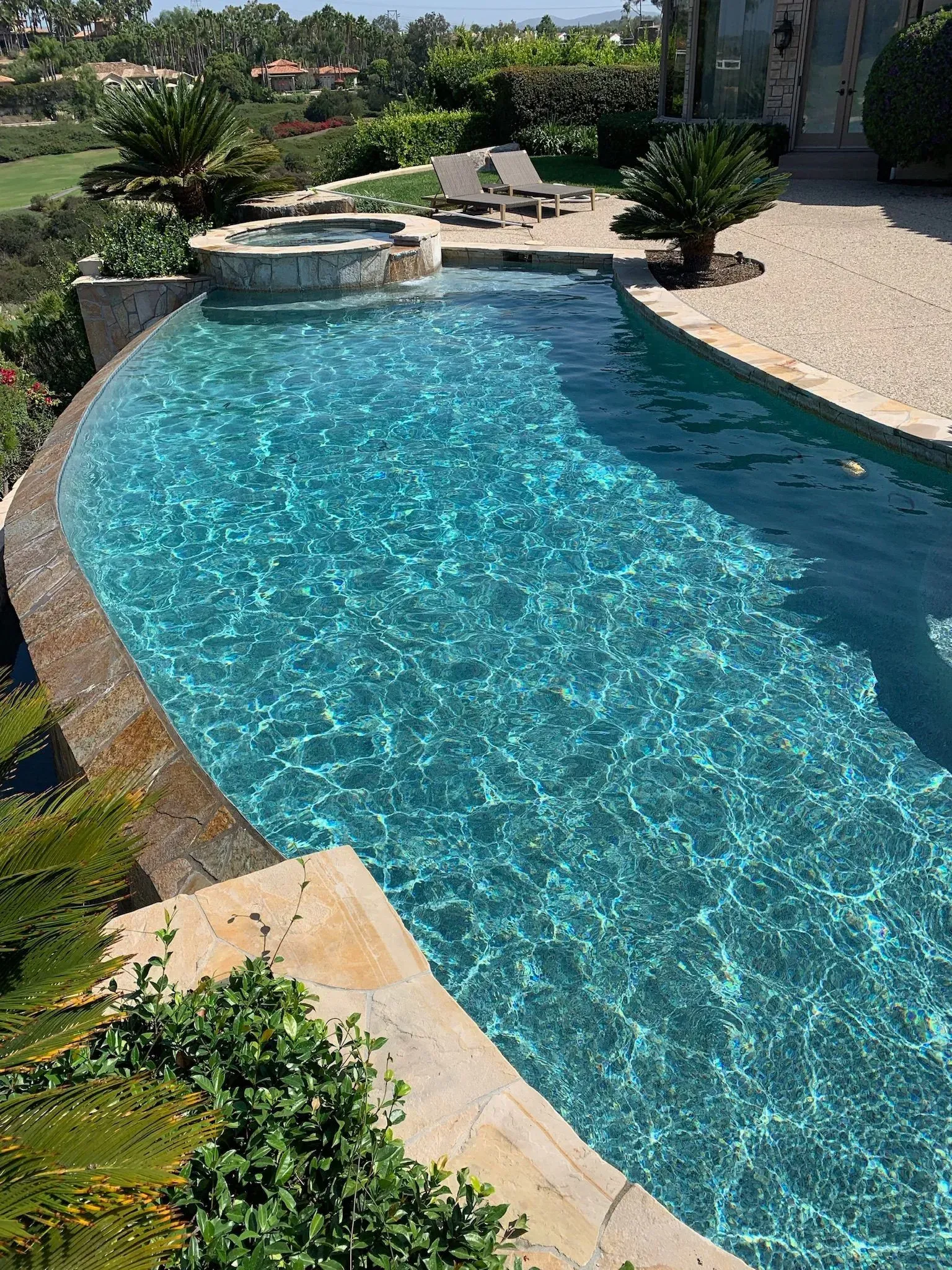 Infinity pool with clear turquoise water, overlooking a lush green landscape.