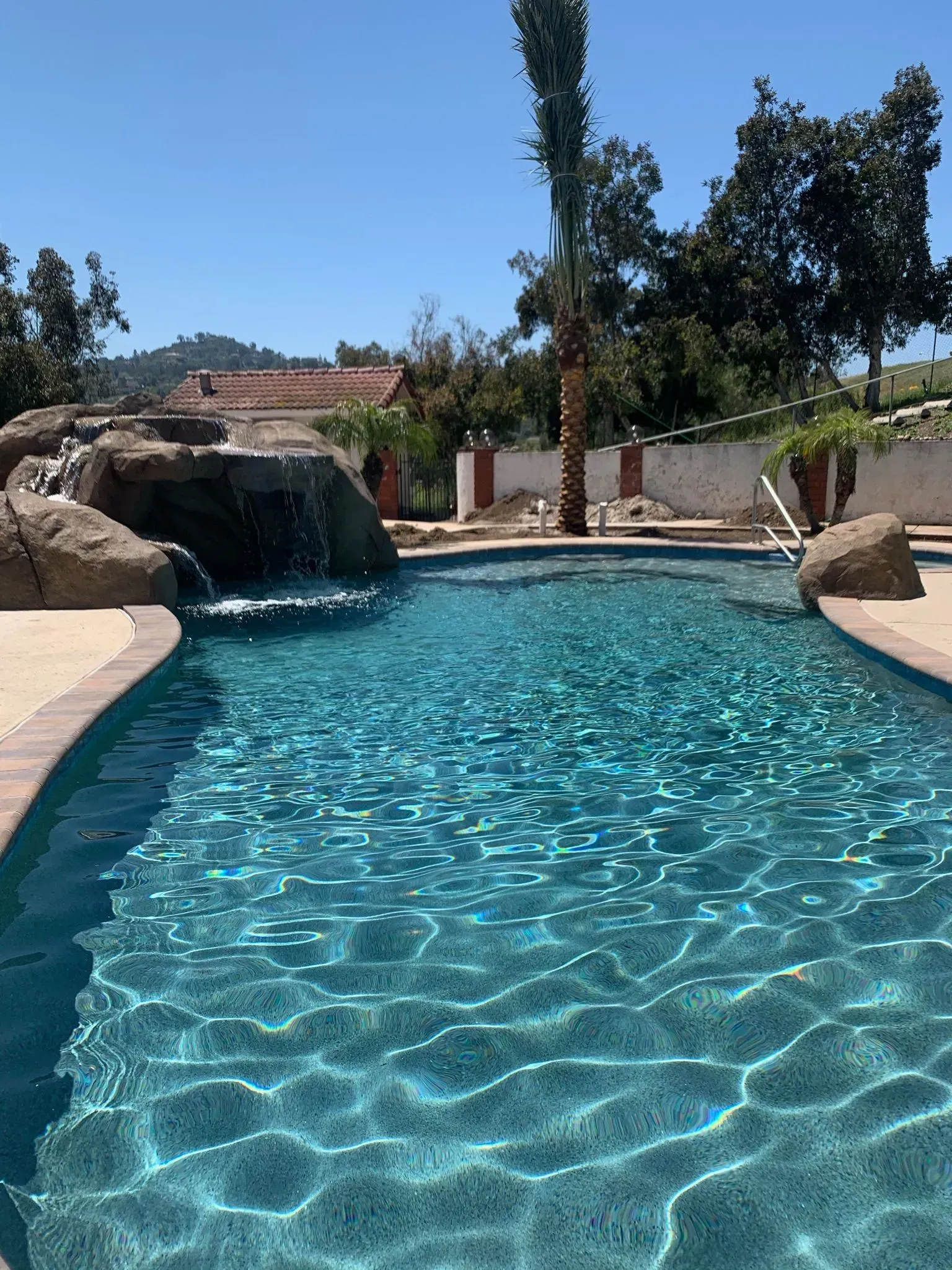 A swimming pool with clear blue water and a waterfall feature on a sunny day.