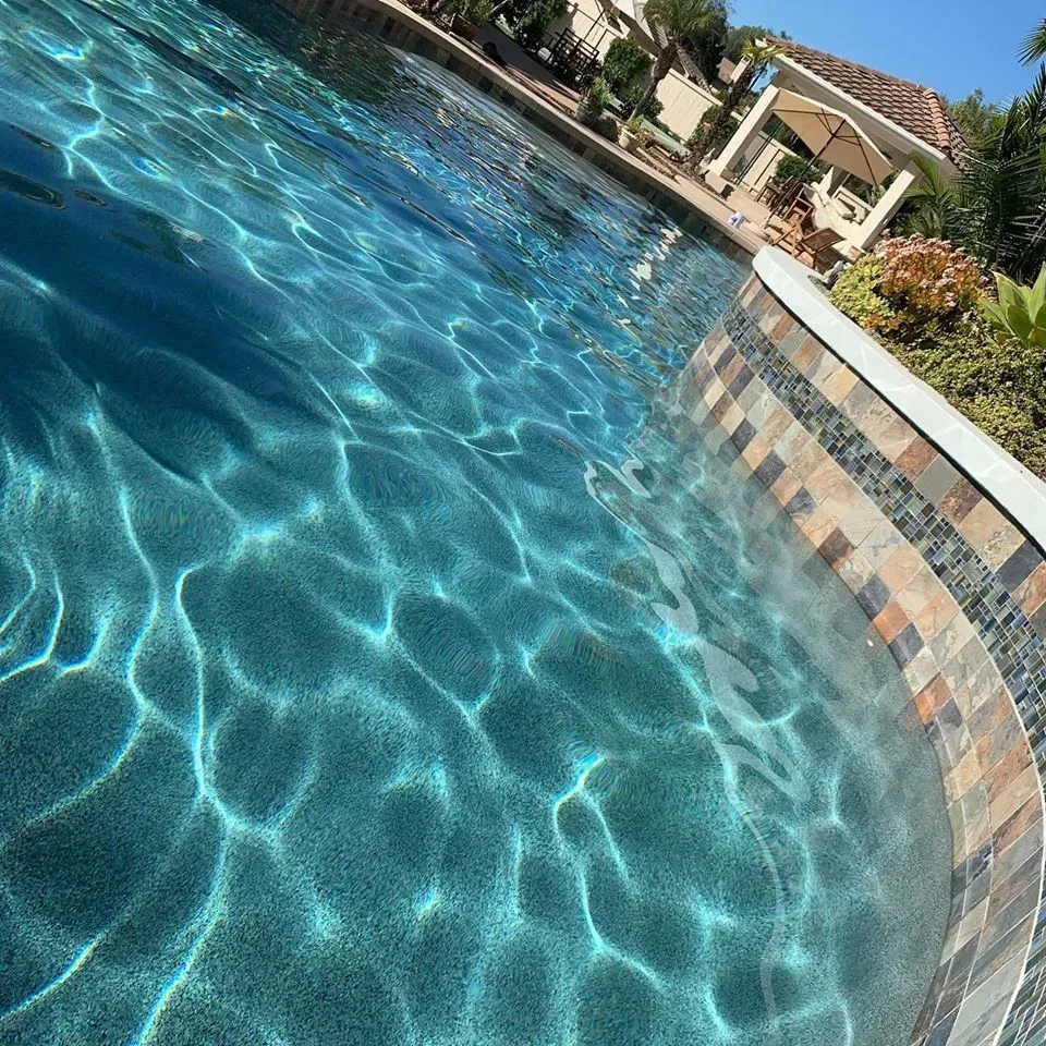 Pool with blue water and stone tile edge, reflecting sunlight.