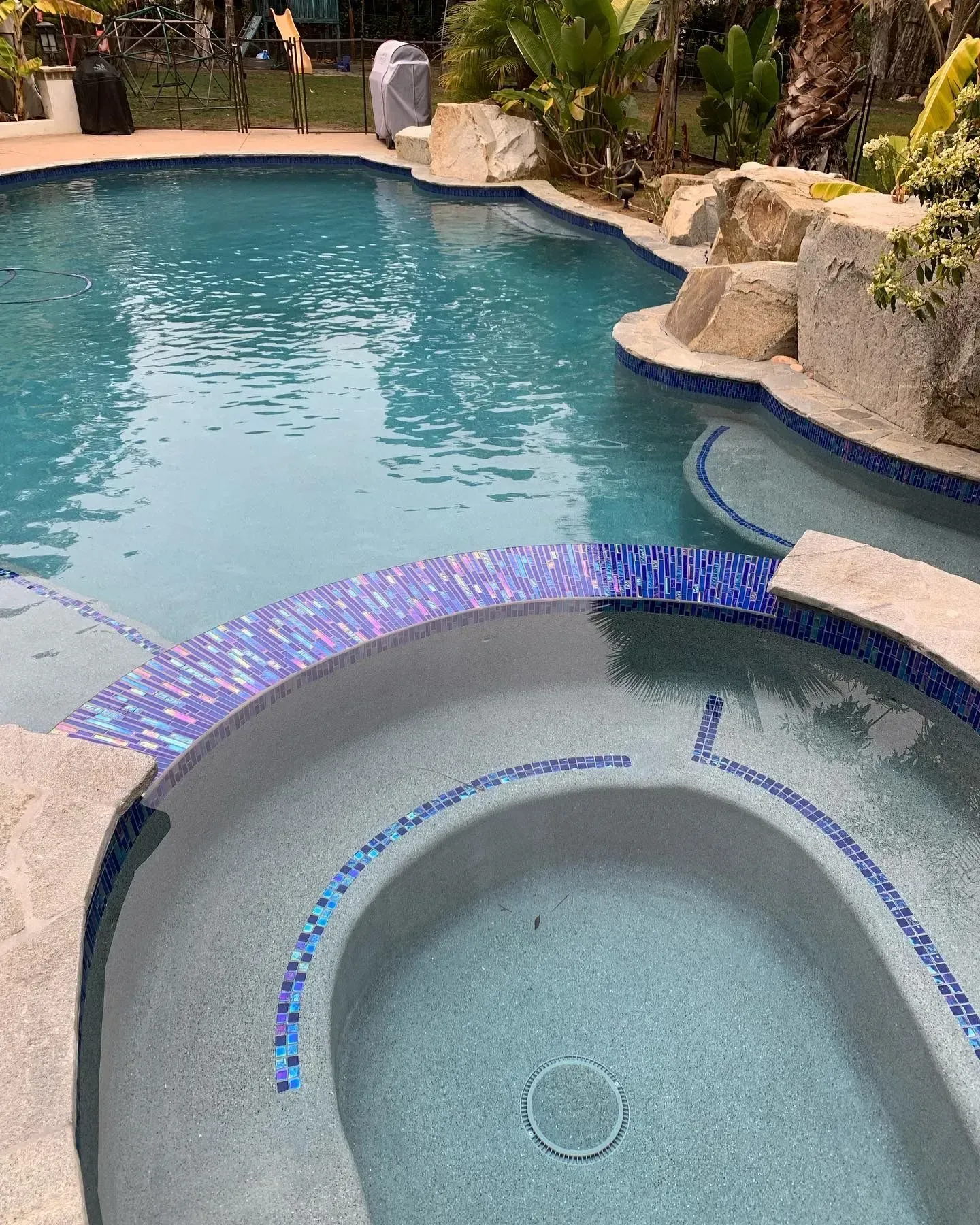 Swimming pool with a blue-tiled jacuzzi and rock features.
