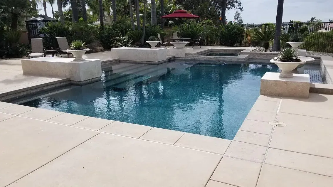 Pool with blue water and light stone surround; steps lead into pool, potted plants nearby.