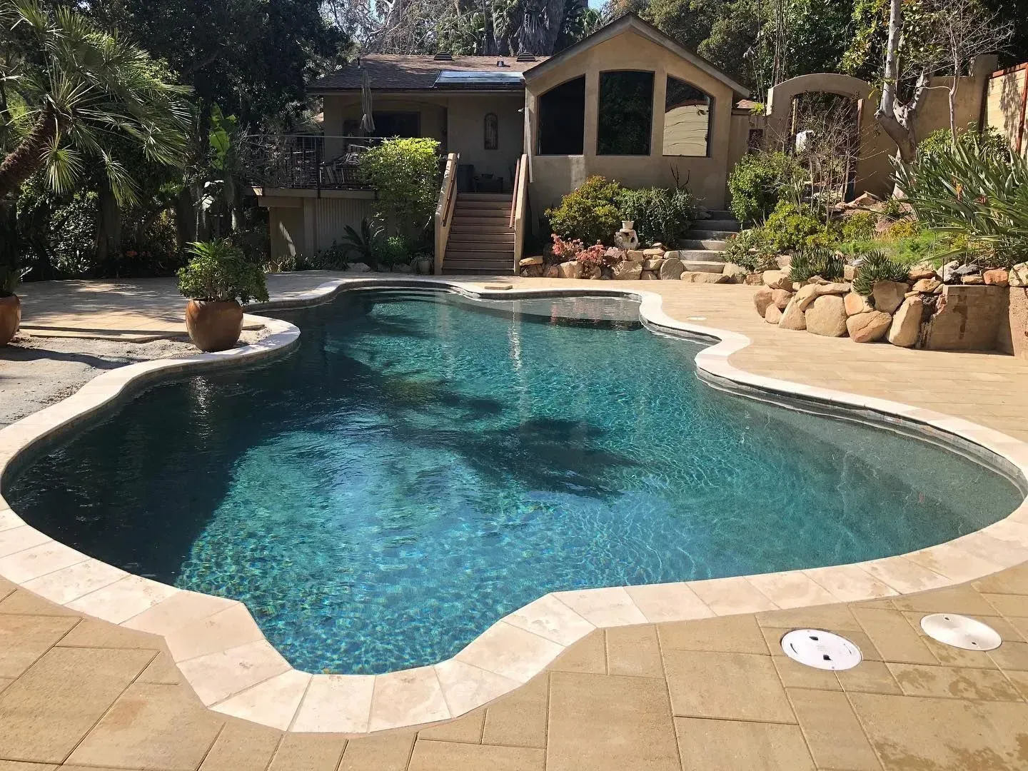 Swimming pool with turquoise water, beige stone surround, and house in background.