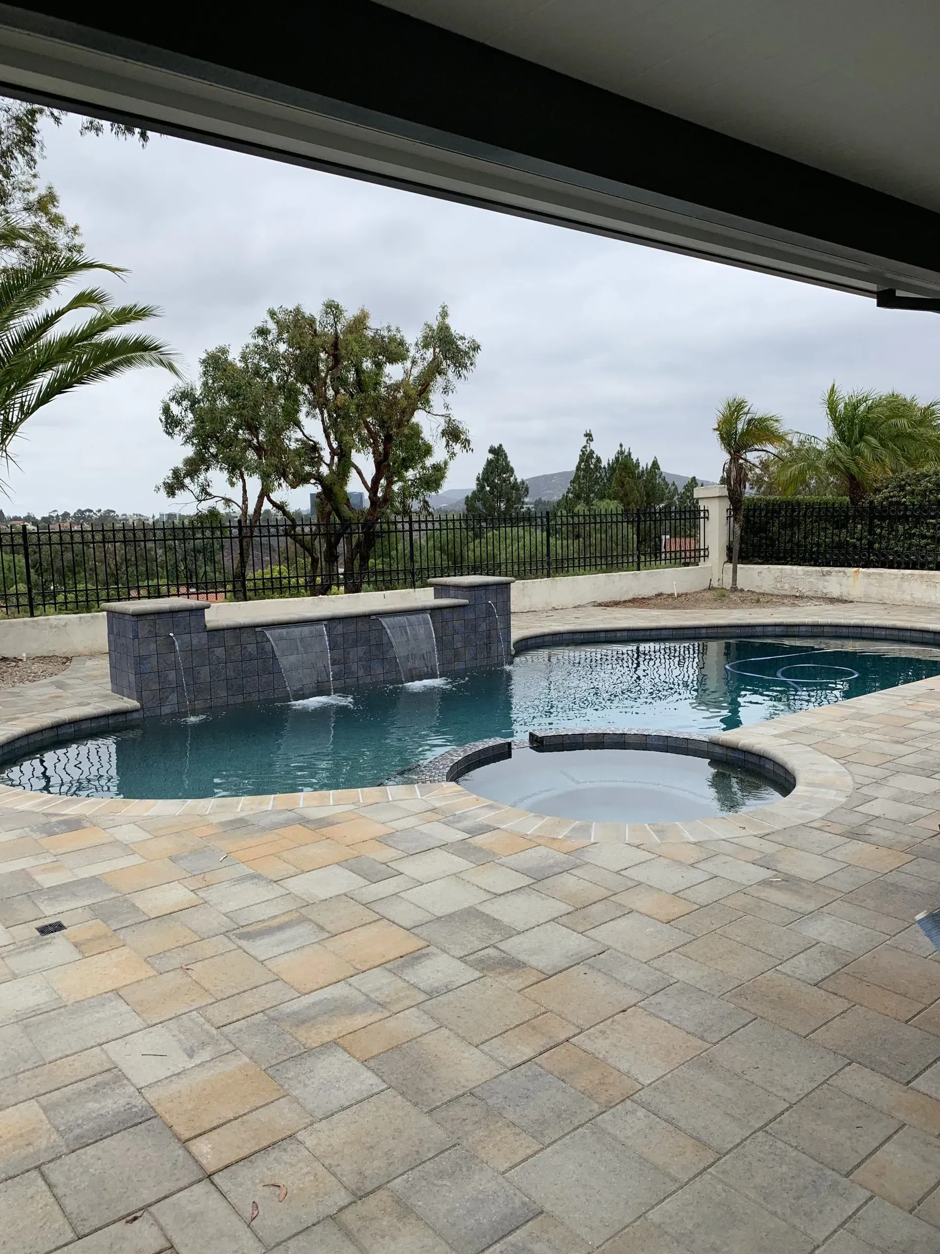 Pool and spa on a paved patio with a water feature.