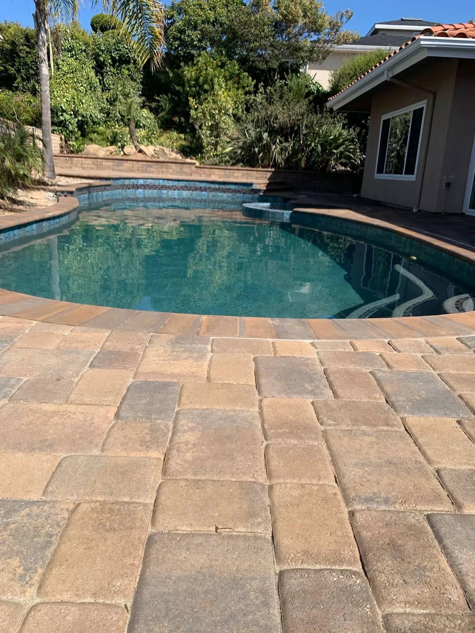 Pool and spa on a paved patio with a water feature.