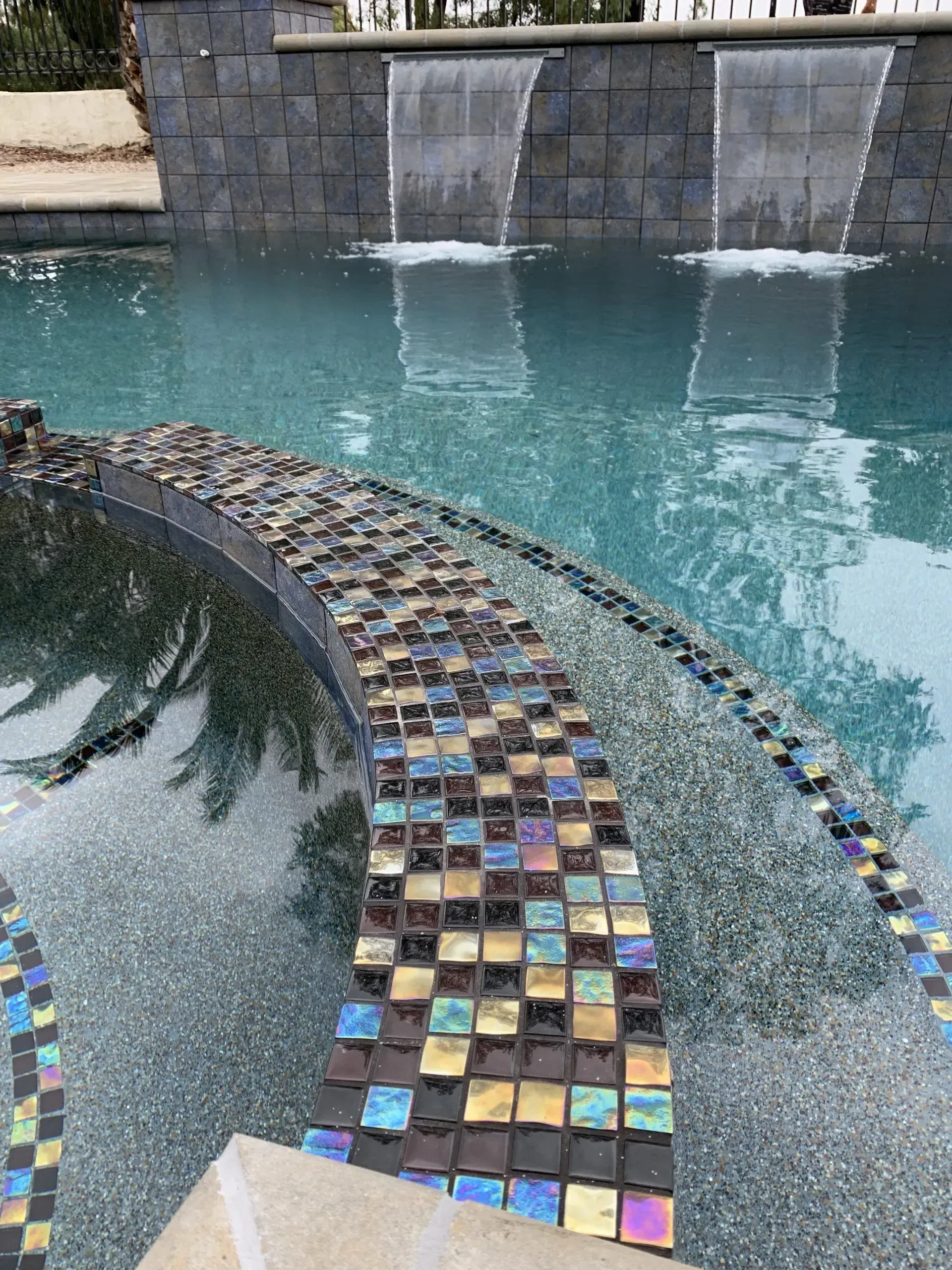 Pool with waterfall feature and mosaic tile detailing.