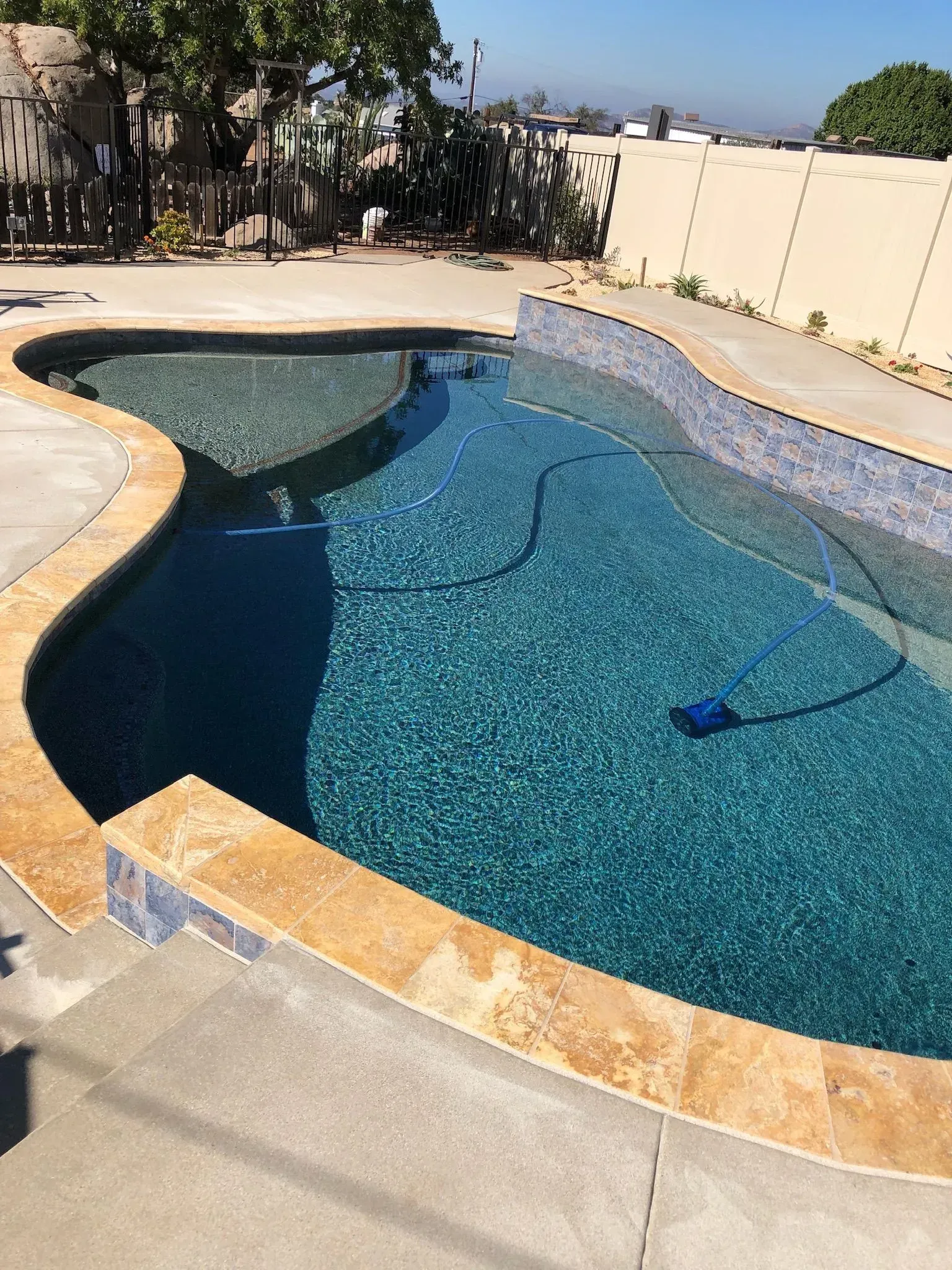 Swimming pool with turquoise water, surrounded by concrete and a beige wall.