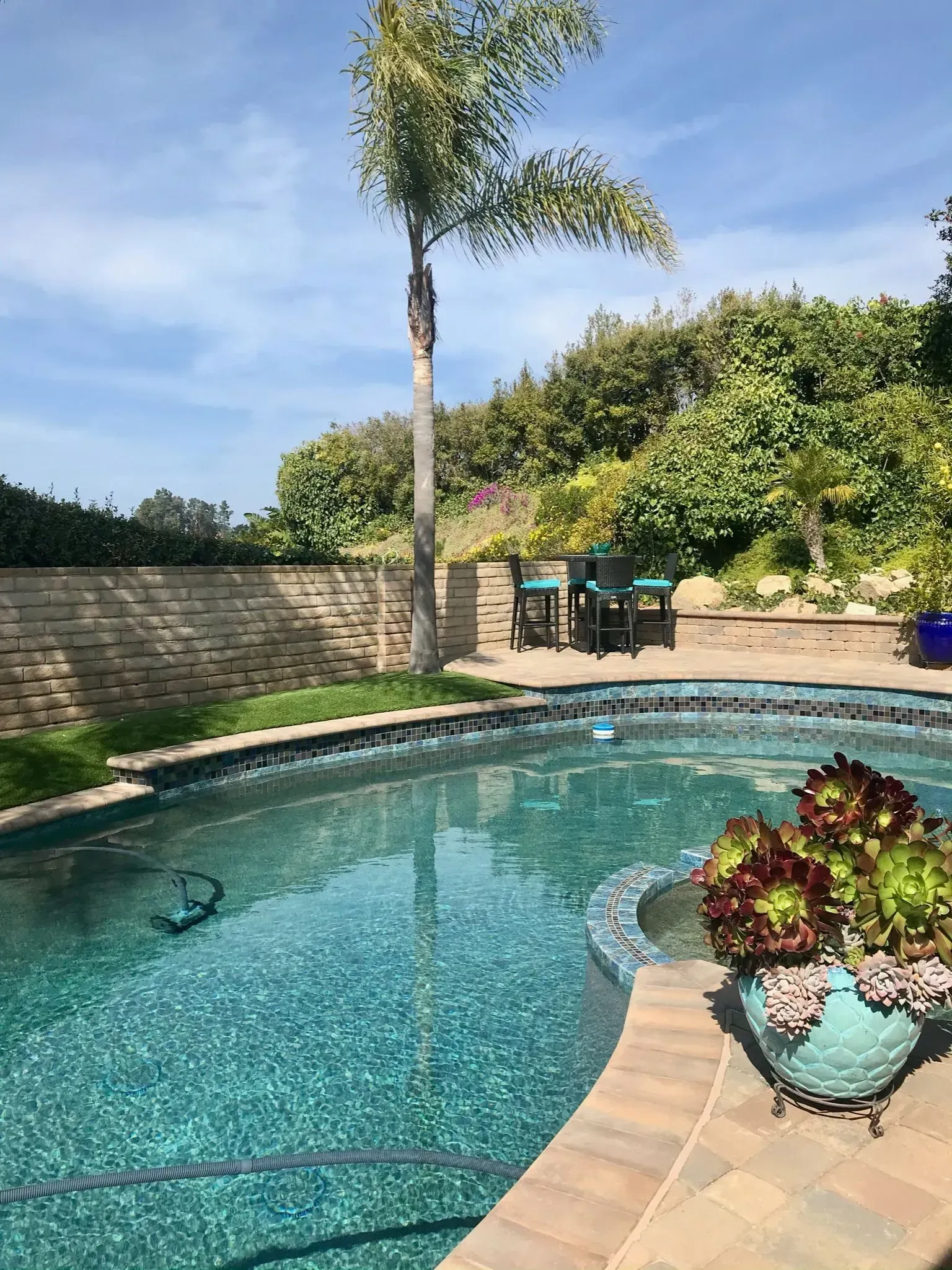 A swimming pool with turquoise water, surrounded by brick and greenery under a sunny sky.