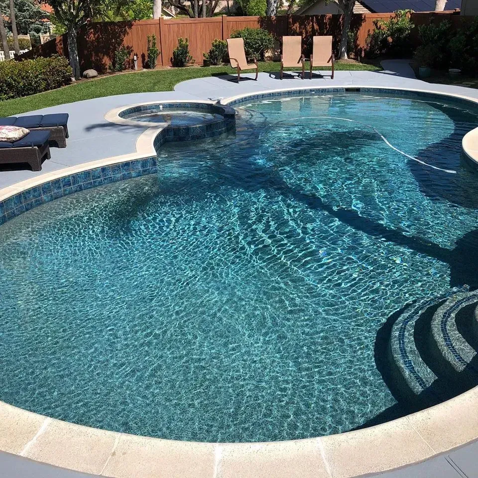 Swimming pool with blue water and steps, surrounded by gray concrete and lounge chairs.