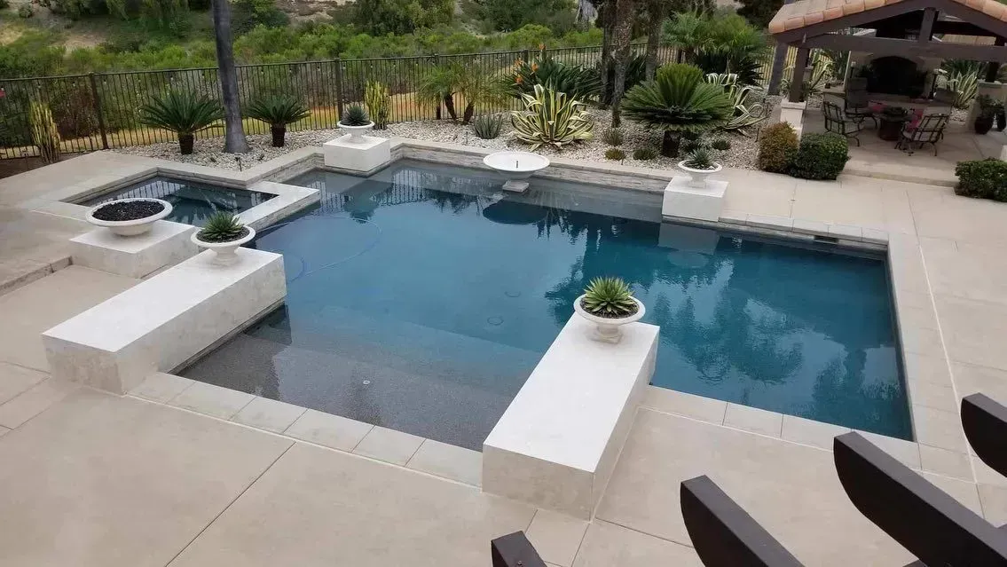 Pool with spa, surrounded by a stone patio with decorative planters and a covered outdoor kitchen.