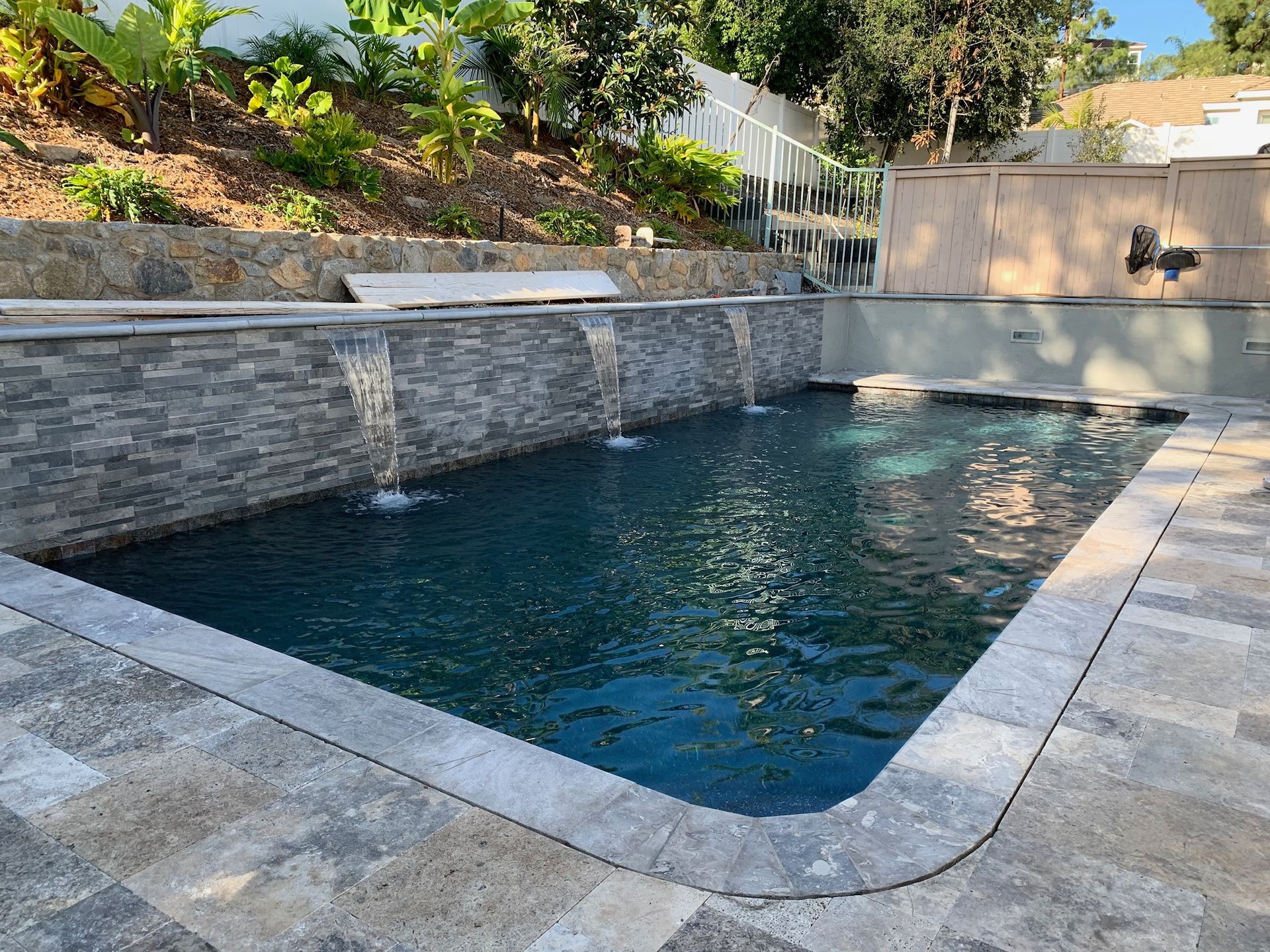 Pool with waterfalls and stone wall in a yard with landscaping.