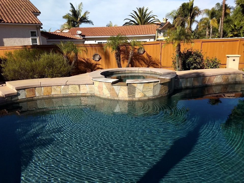Swimming pool with attached hot tub, stone and wood surround, sunny outdoor setting.