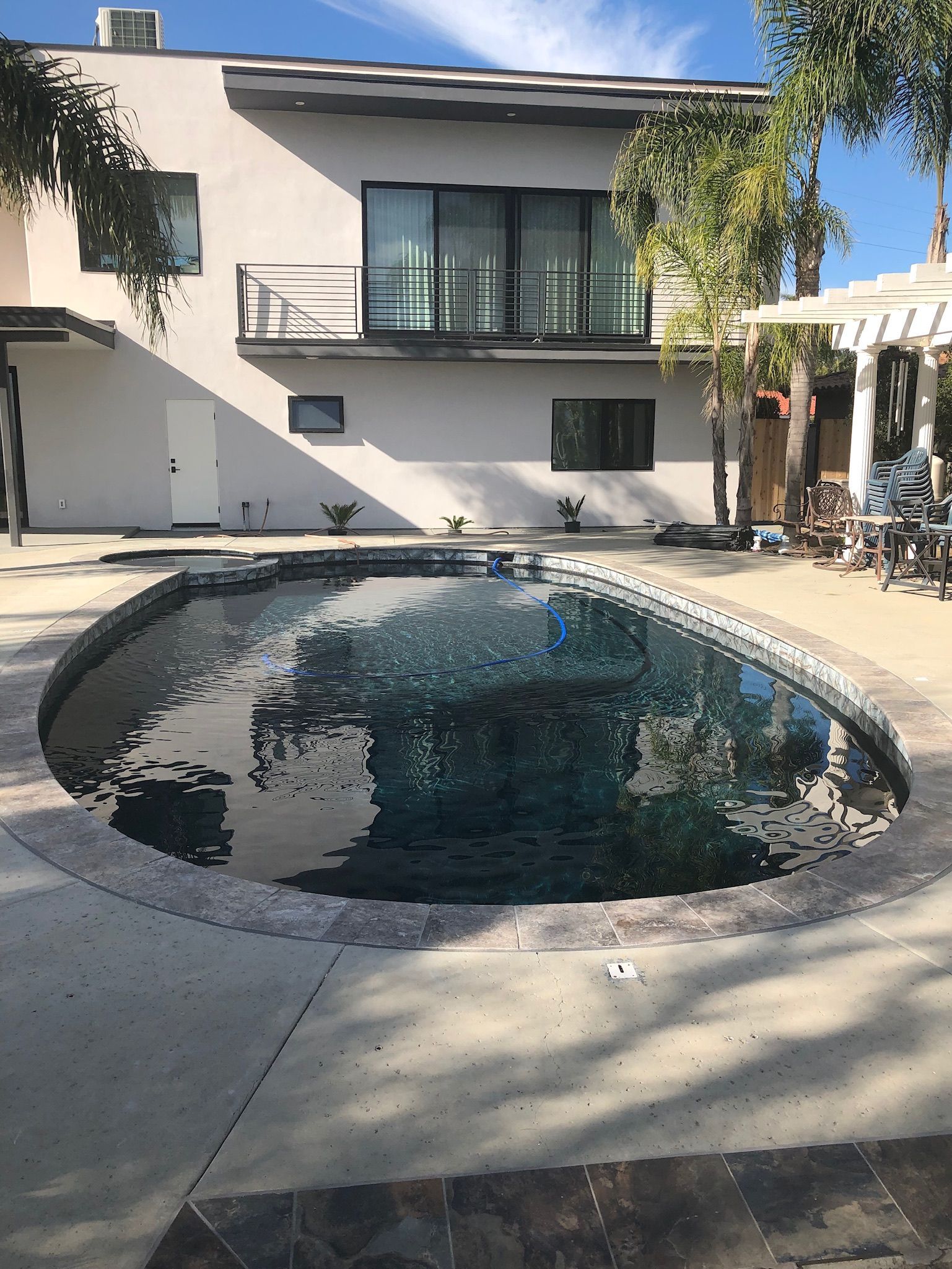 Backyard with a dark pool and a two-story light stucco house with a balcony.