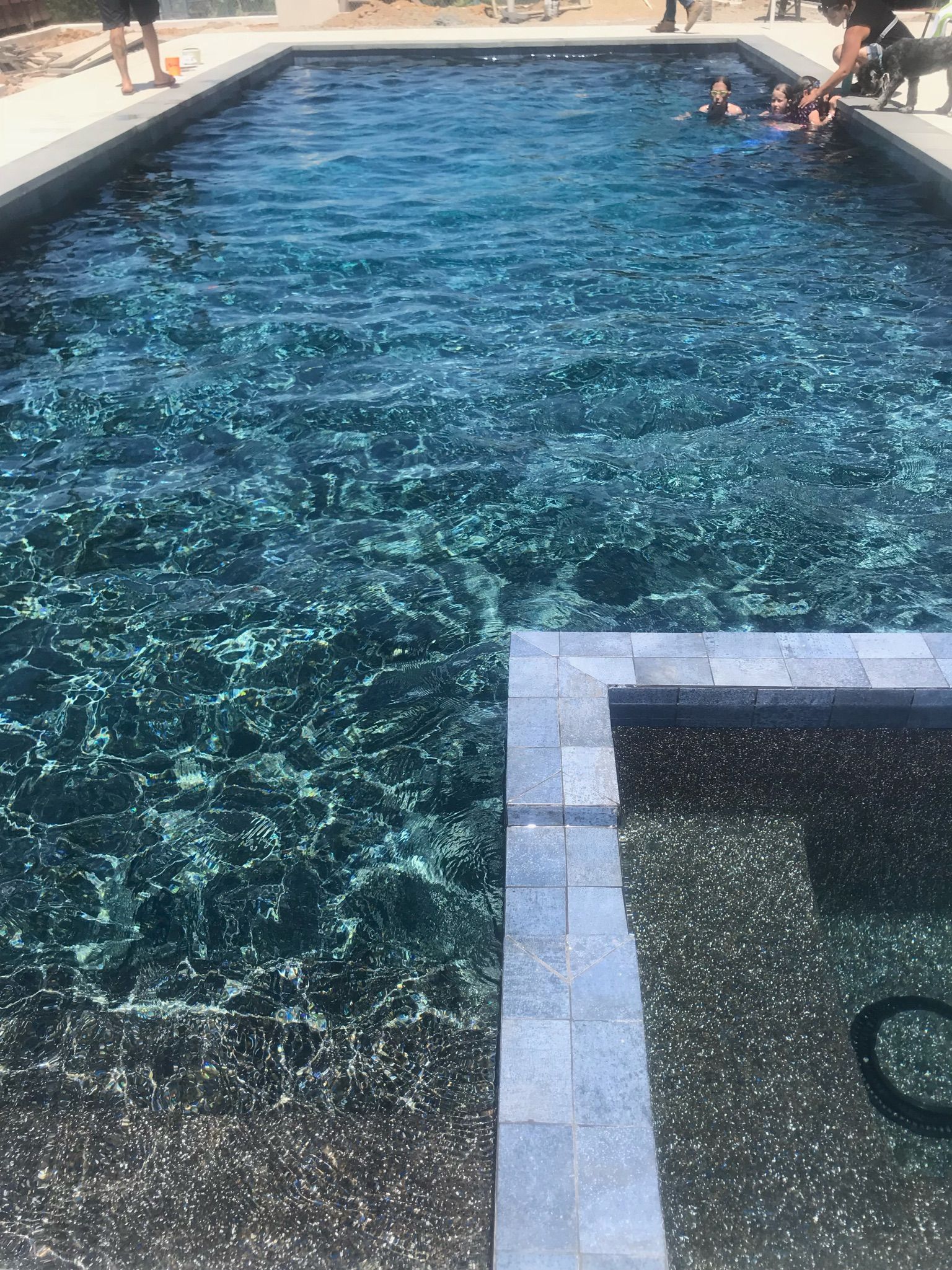 Rectangular pool with dark water; people swim near the edge. Gray stone border and steps.