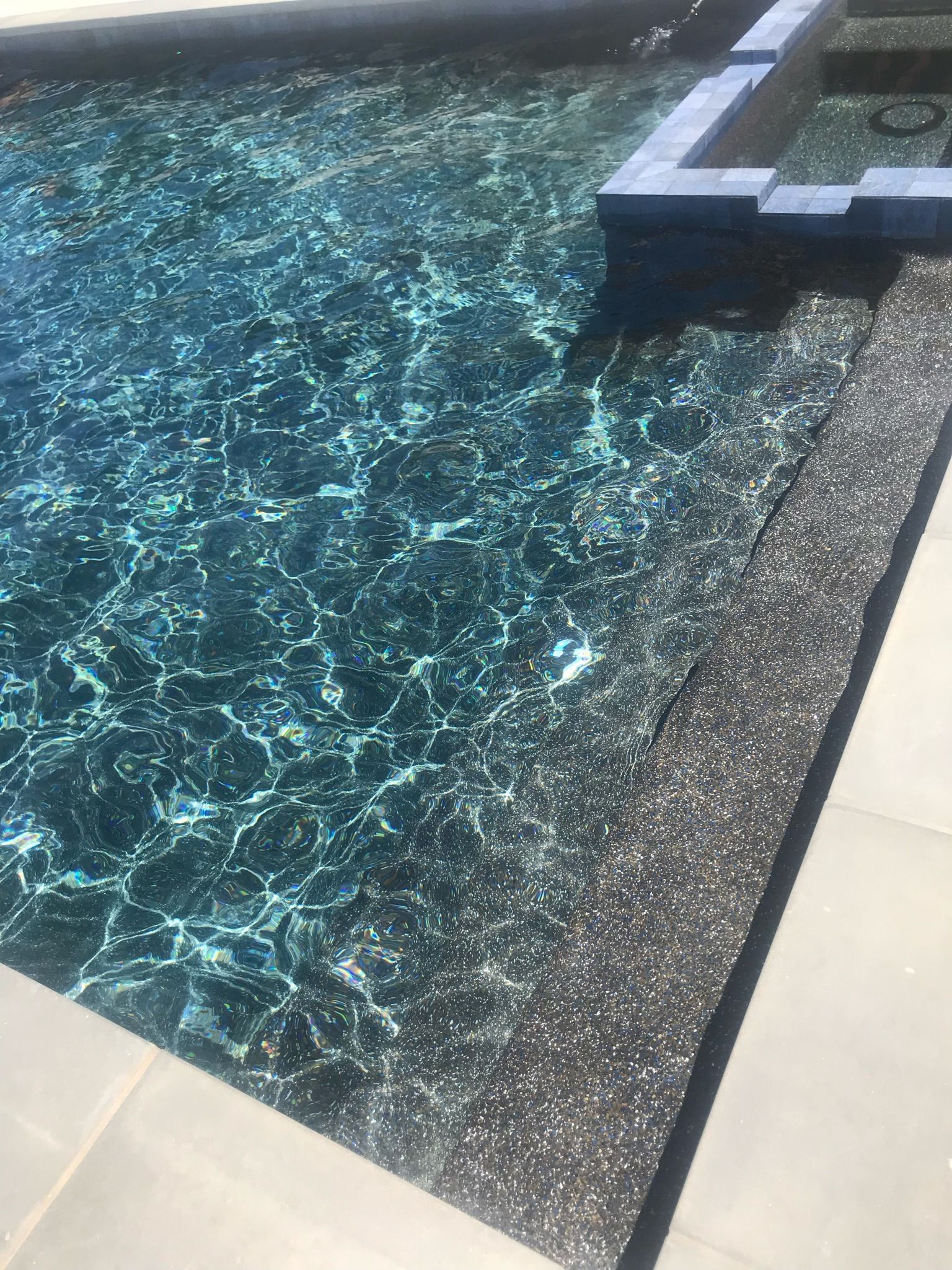 Dark blue swimming pool with stone steps and light-colored tiled surround.
