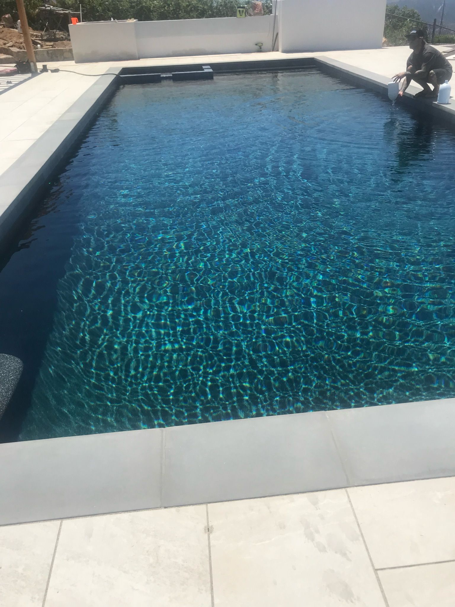 A rectangular swimming pool filled with turquoise water, a person near the edge.
