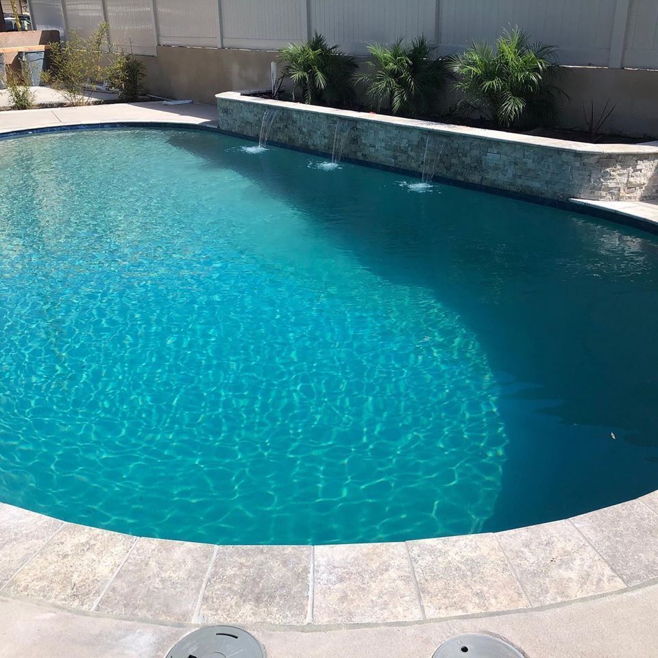 Pool with turquoise water, a stone wall with water features, and palm trees.