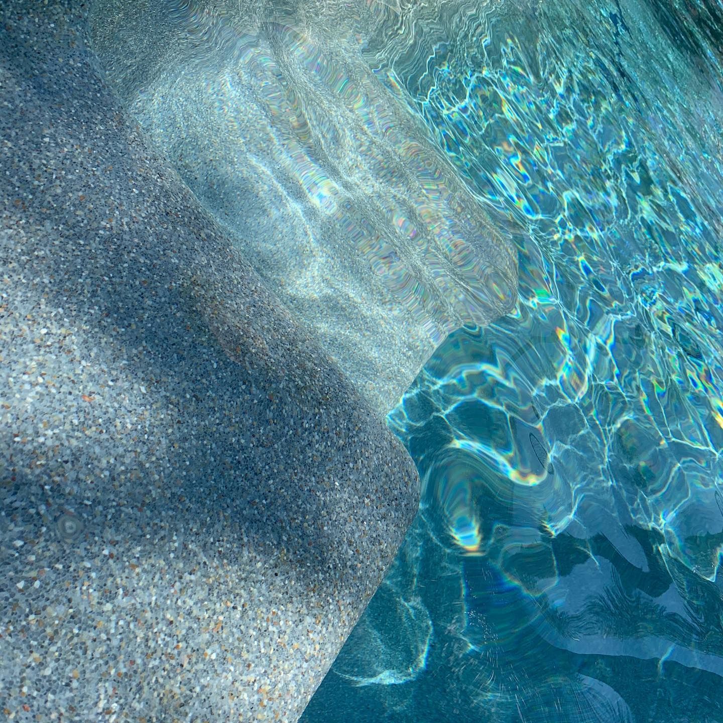 Close-up of a pool with textured grey steps and shimmering turquoise water.