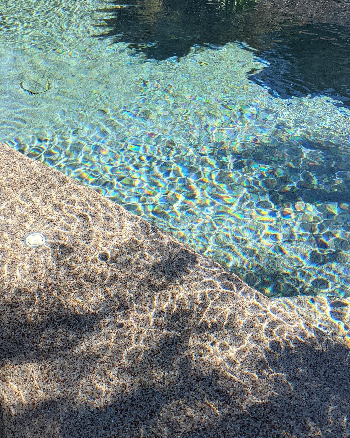 Close-up of a pool with clear, sparkling turquoise water reflecting sunlight against a textured, stone-like edge.