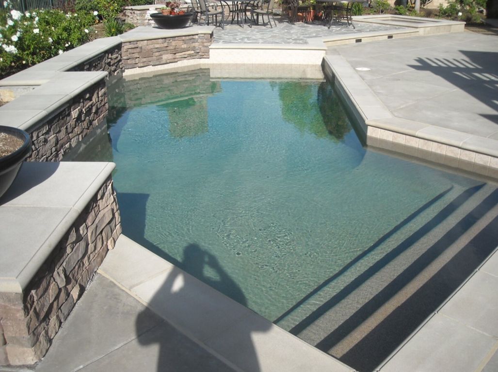 Small outdoor plunge pool with stone and concrete surround. Steps lead into the water.