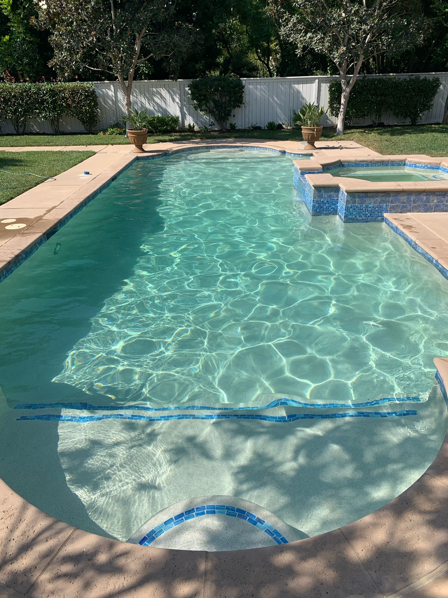 Swimming pool with turquoise water, surrounded by concrete and landscaping, under a sunny sky.