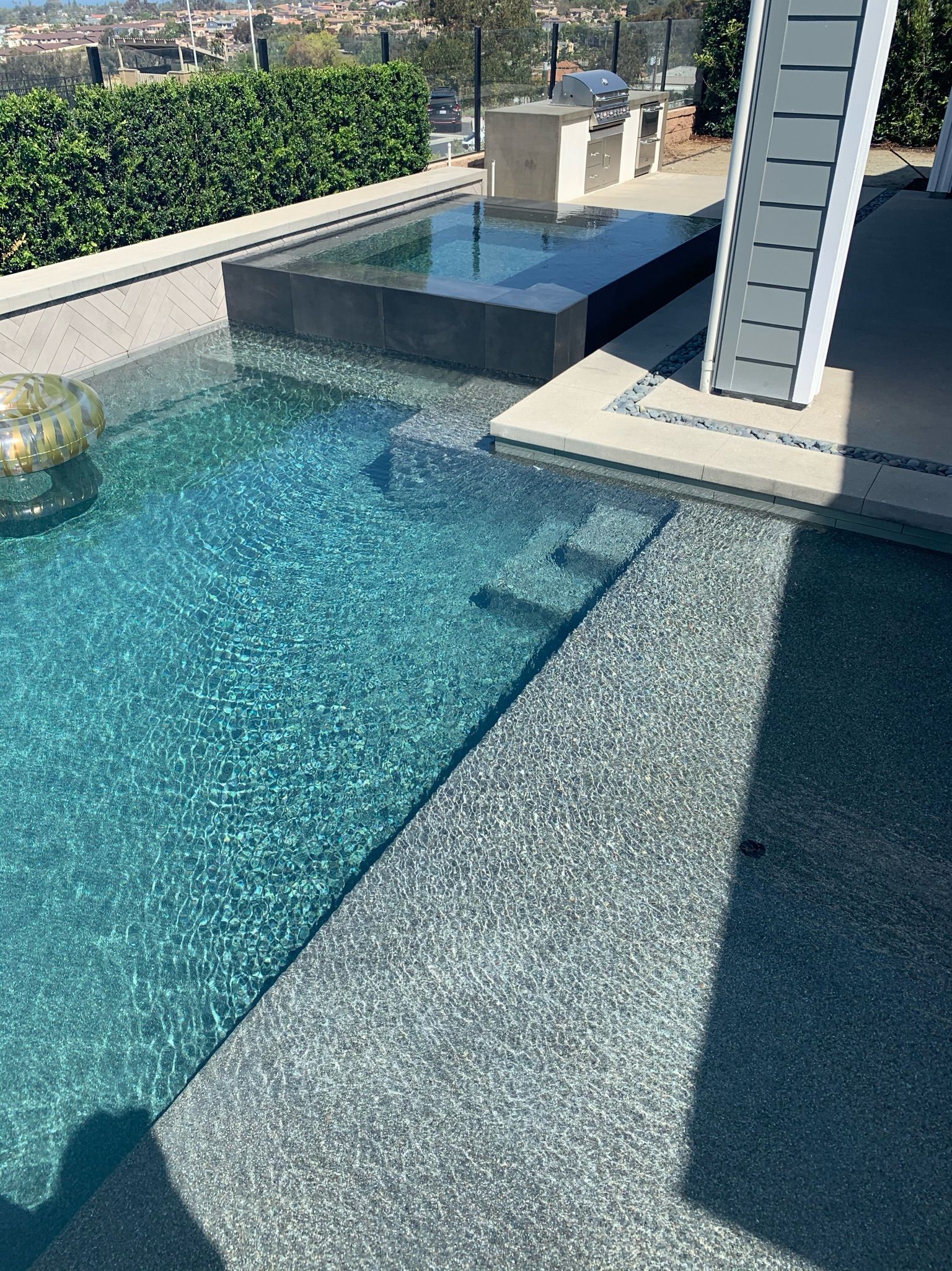 Pool with turquoise water, steps, and a dark raised edge. Sunny outdoor setting.