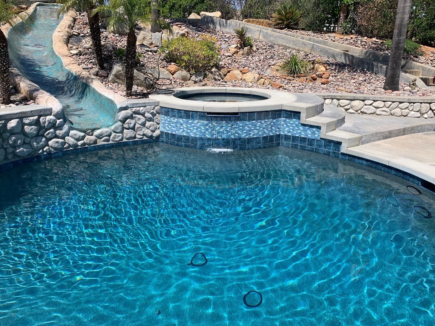 Pool with waterslide, spa, and landscaping. The water is blue.