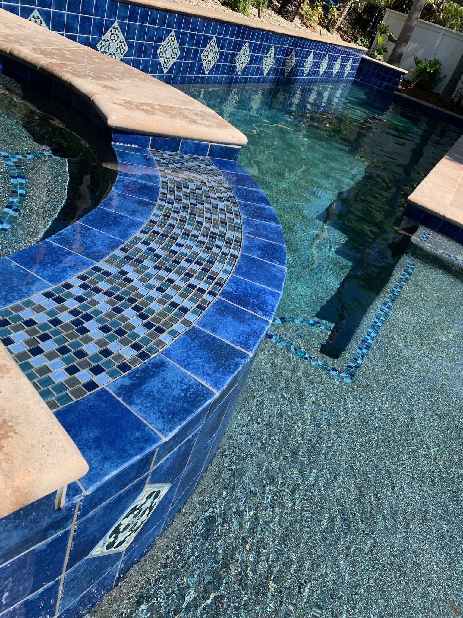 Blue tiled swimming pool with mosaic detail, steps, and surrounding concrete.