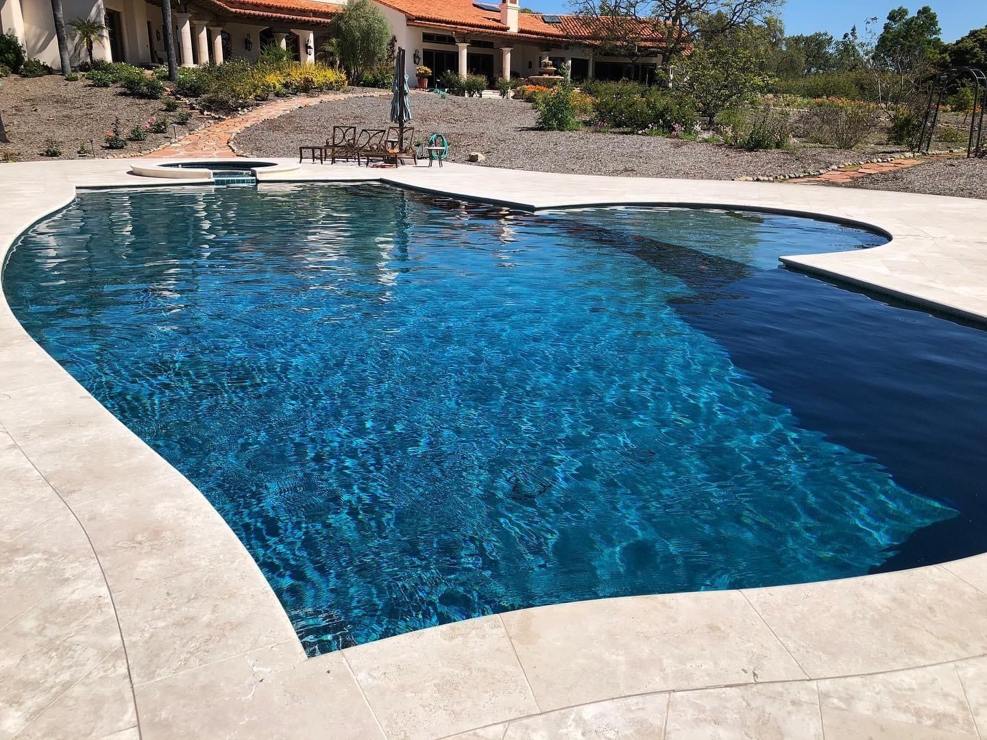 Swimming pool with blue water and stone deck. House in the background.