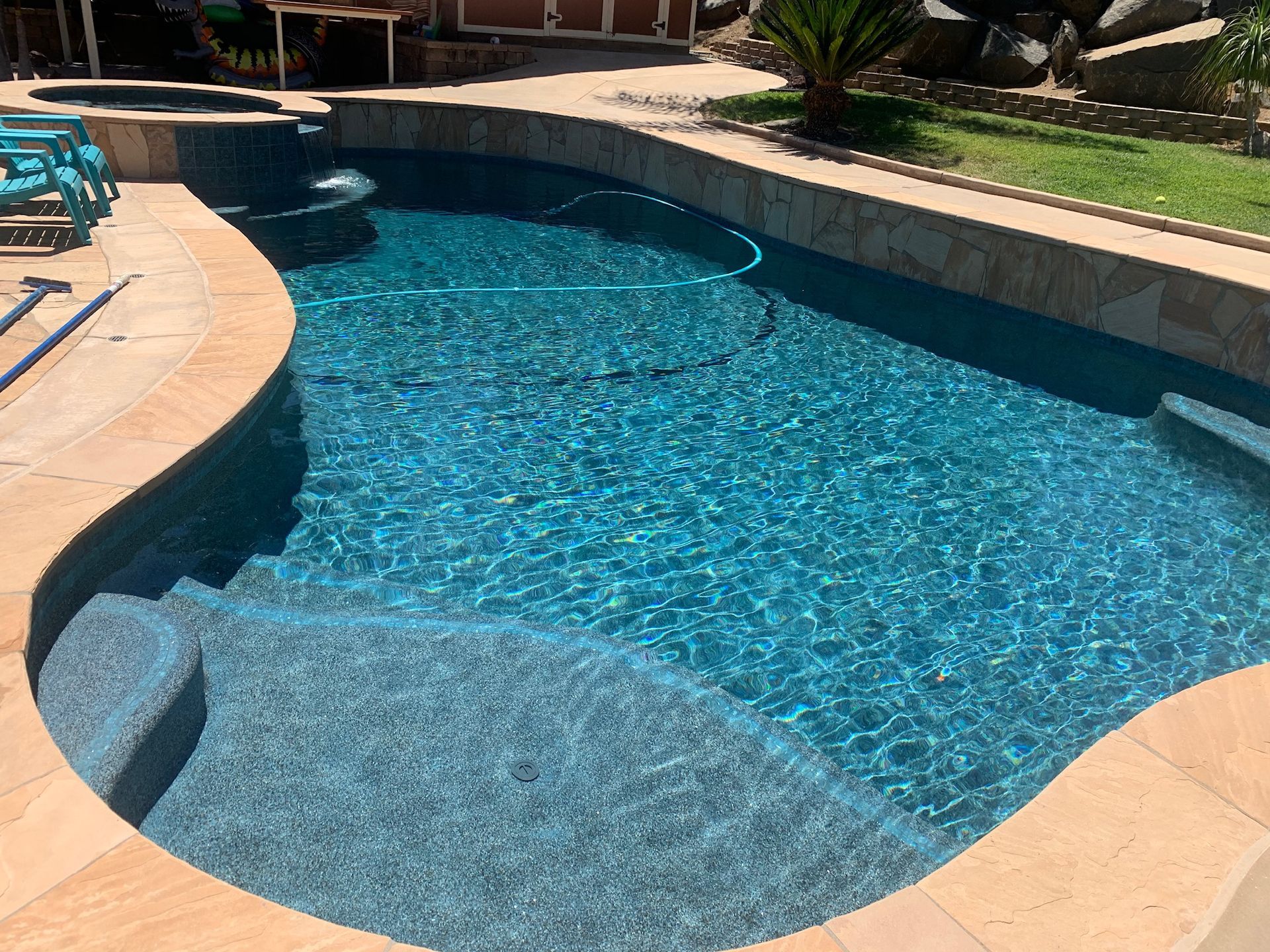 A blue-tiled swimming pool with stone steps and edging in a backyard setting.