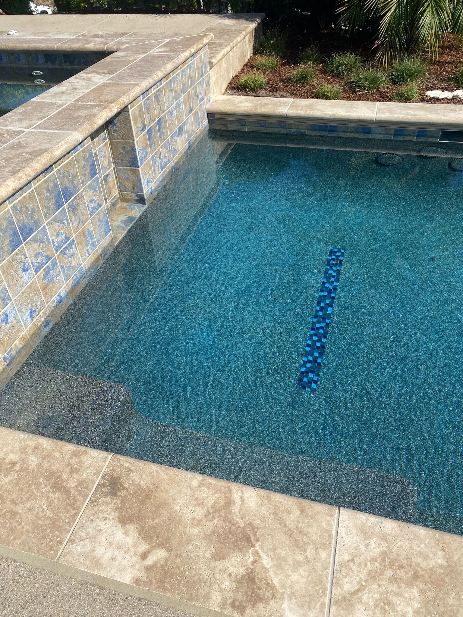 Pool with a blue-tiled wall and light blue water, surrounded by concrete.