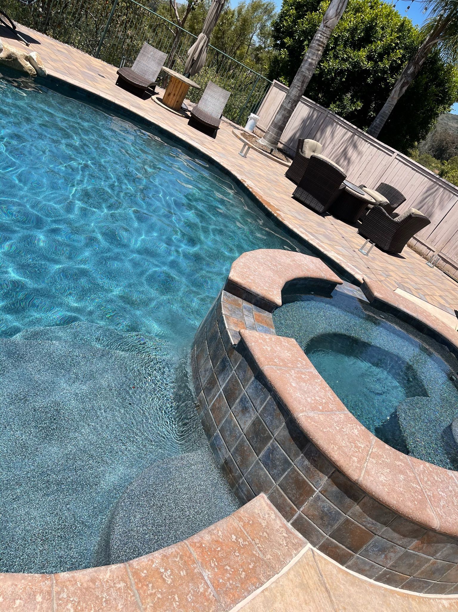 Pool with turquoise water and a spa, surrounded by stone and a sunny outdoor setting.
