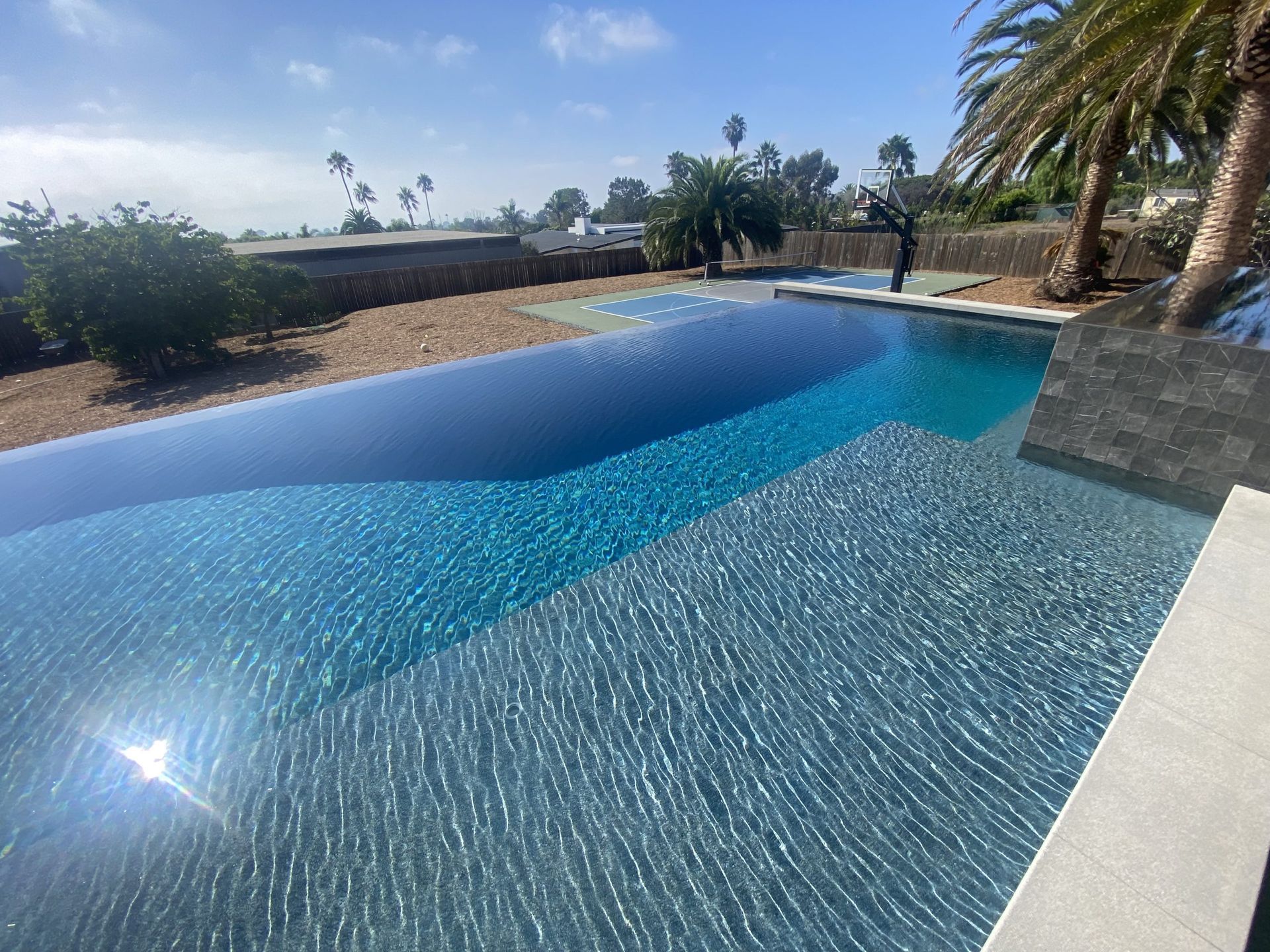 Infinity pool with varying shades of blue water, palm trees, and clear sky.