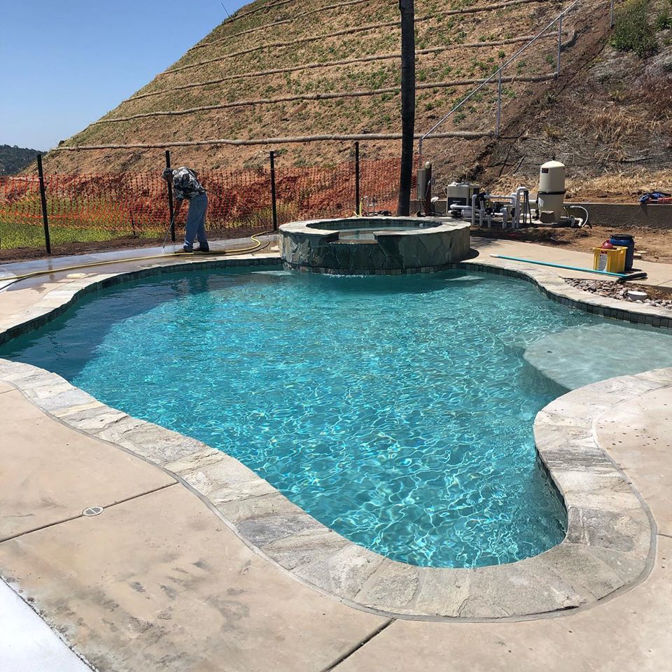 Pool with turquoise water, a hot tub, and a person working on the side in a sunny setting.